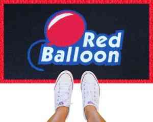 Dois pés com tênis branco pisam sobre um tapete para comércio com o logotipo da empresa Red Balloon